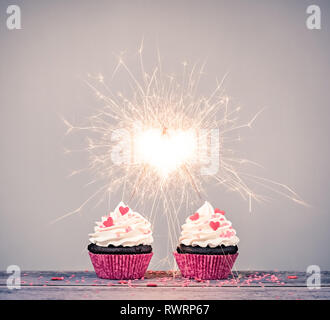 Two valentines day buttercream Cupcakes with sparklers creating a heart shape celebrating love concept Stock Photo
