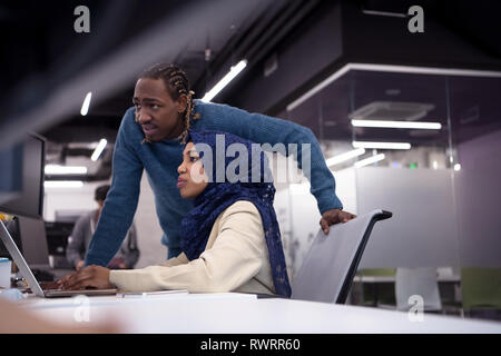 black muslim female software developer working together with her african american male colleague using computer while writing programming code at mode Stock Photo