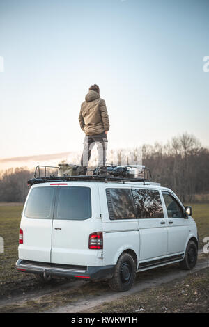 Young man standing on the roof of a van surrounded by nature Stock Photo