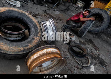 A Colombian wheel mechanic works on tires in front of a car repair shop in Barrio Triste, Medellín, Colombia. Stock Photo
