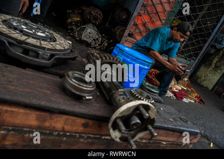 A Colombian car mechanic reads a mobile phone screen in front of a car repair shop in Barrio Triste, Medellín, Colombia. Stock Photo