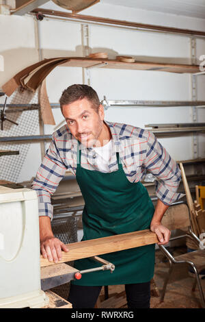 Young man as a carpenter or carpenter with wood beams at the planing machine Stock Photo