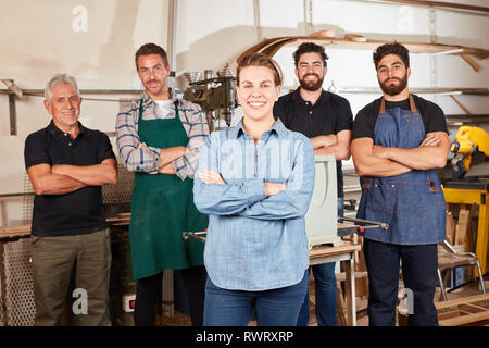 Smiling woman as apprentice in carpentry in front of carpenter colleagues in workshop Stock Photo