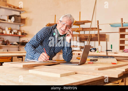 Senior craftsman using laptop computer and cellphone in joinery workshop Stock Photo