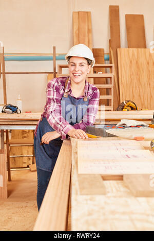 Happy young woman with blueprint and helmet as a craftsman apprentice in joinery Stock Photo