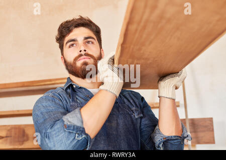 Young man as carpenter or carpenter in training carries wooden beams Stock Photo