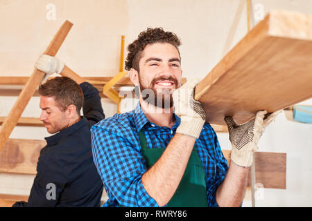 Young man as a carpenter or carpenter apprentice carries wood beams in the workshop Stock Photo