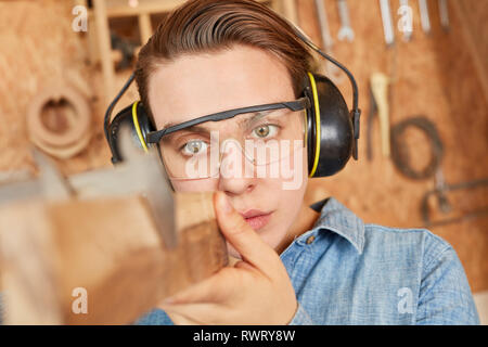 Woman as a carpenter apprentice while measuring wood board with caliper Stock Photo