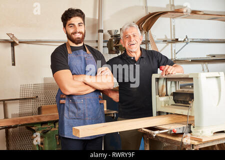 Happy carpenter team is working with wood at a planing machine in the workshop Stock Photo