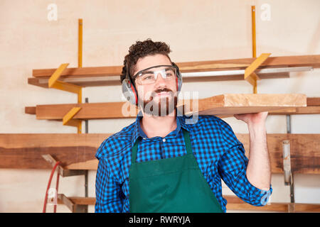 Young man as a carpenter or carpenter apprentice carries wood beams in the workshop Stock Photo