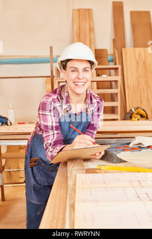 Smiling young woman as a craftsman apprentice with clipboard in joinery Stock Photo