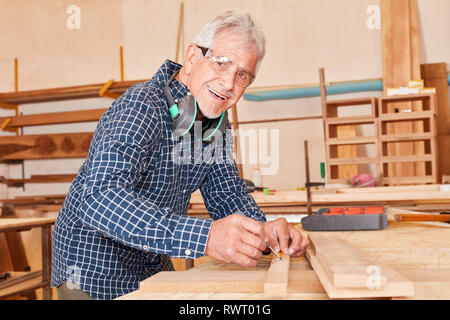Senior man as a carpenter with experience at the workbench when measuring wood Stock Photo