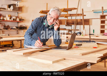 Old craftsman is talking on the phone in his carpentry workshop Stock Photo