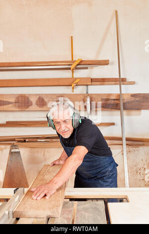 Senior man as a carpenter at work on the circular saw in the carpentry workshop Stock Photo