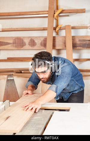 Young carpenter apprentice with ear protection saws wood at the circular saw in the workshop Stock Photo