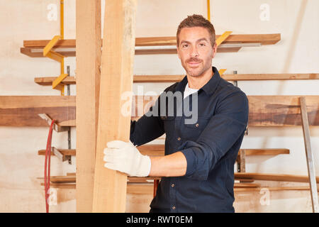 Young craftsman as a carpenter apprentice carries wooden beams in the workshop Stock Photo