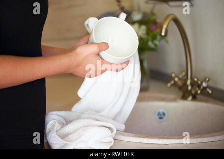 Close up of young woman drying dishes in kitchen with the towel Stock Photo