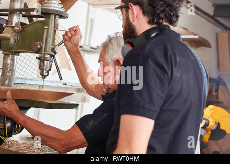 Apprentice observes senior carpenter while working with wood on drill Stock Photo