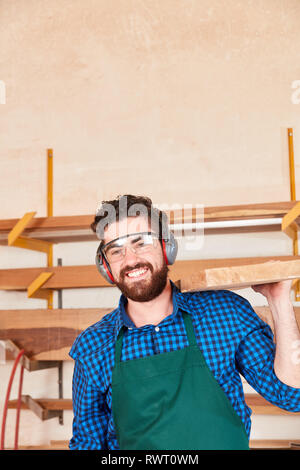 Young man with ear protection as a carpenter apprentice carries a wooden beam Stock Photo