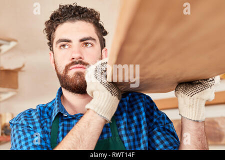 Young man as carpenter in training carries wooden beams in joinery Stock Photo