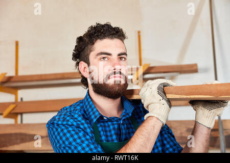 Man as a worker or joiner apprentice carries a joist in the joinery Stock Photo