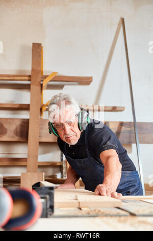 Senior as a carpenter Master works on the circular saw in the carpentry workshop Stock Photo
