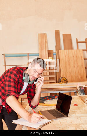 Young man as a craftsman using mobile phone and laptop computer while scheduling Stock Photo
