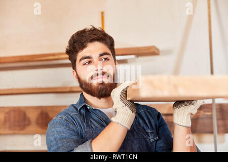 Young worker or carpenter carries a beam in joinery or joinery Stock Photo