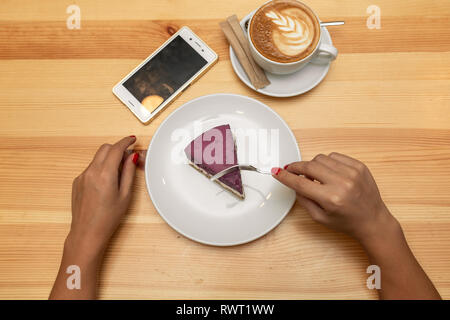 View from above on woman hands on wooden table hold coffe cup near cheesecake and smartphone. Stock Photo