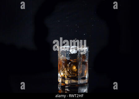 https://l450v.alamy.com/450v/rwt2hf/big-splash-with-drops-of-whisky-from-the-glass-of-beverage-with-fallen-ice-cube-into-glass-isolated-on-reflective-black-surface-rwt2hf.jpg