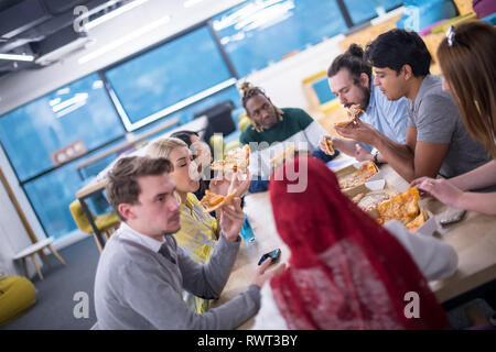 Friendly diverse multiethnic business team eating sharing pizza together in startup office, multiracial coworkers staff group enjoying break talking l Stock Photo