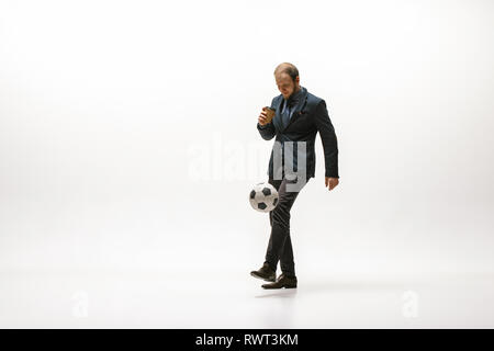 Businessman with a cup of coffee and football ball in office. Soccer freestyle. Concept of balance and agility in business. Manager perfoming tricks isolated on white studio background. Stock Photo