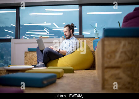 software developer writing programming code using laptop computer while sitting on lazy bag in modern startup office Stock Photo