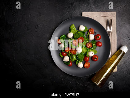 Salad with mozzarella and baby spinach on black ceramic plate olive oil with Parmesan and herbs in the bottle., Copy space. Stock Photo