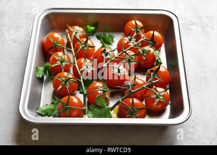Close up of roasted cherry tomatoes in baking tray on light stone background Stock Photo
