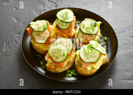 Sandwiches with salmon, scrambled eggs and cucumber slices on black stone background Stock Photo