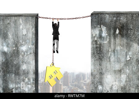 Businessman shackled by gold house hanging on iron chains connected two concrete walls. Stock Photo