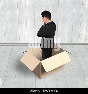 Man thinking in the opened box, on wooden wall and floor indoors background. Stock Photo