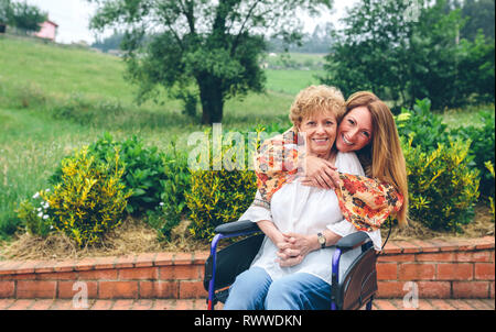 Daughter embracing her senior mother in wheelchair Stock Photo