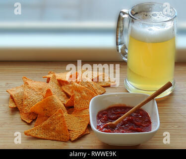 Glass of beer, nachos and salsa in white dish with wooden spoon on wooden board Stock Photo