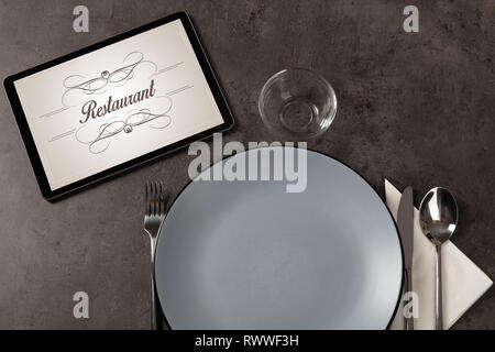 Tablet with stylish restaurant logo and laid table  Stock Photo
