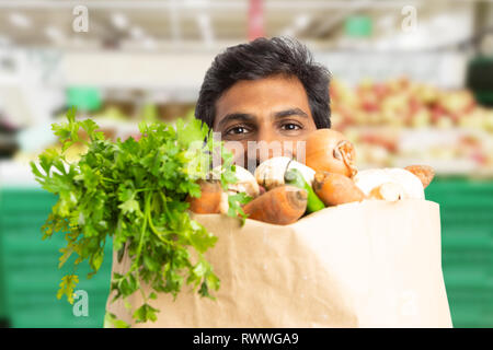 Close-up of indian male supermarket or hypermarket employee hiding behind grocery paper bag Stock Photo