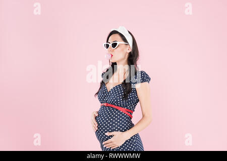 Pregnant woman in sunglasses chewing bubble gum isolated on pink Stock Photo