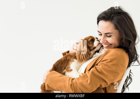 Happy laughing girl in brown jacket holding dog isolated on white Stock Photo
