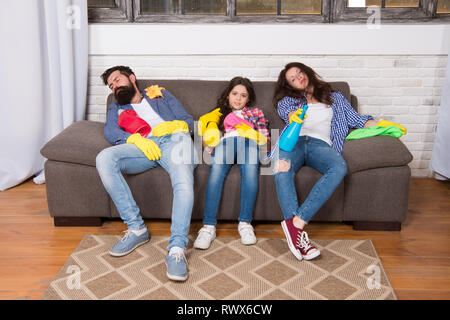 Finish cleaning. Cleaning all day exhausting occupation. Tired parents and kid. Exhausting cleaning day. Family mom dad and daughter with cleaning supplies sit on couch. Family care about cleanliness. Stock Photo