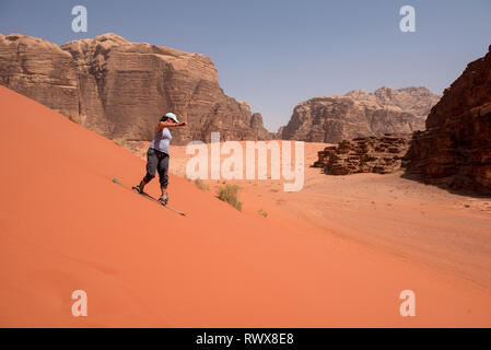 WADI RUM, JORDAN - MAY 18, 2018: Girl sandboarding on the red sand dunes of the desert Stock Photo