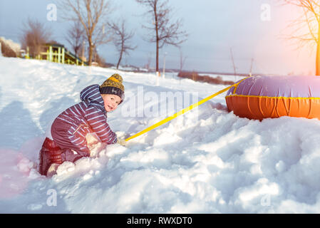 Little boy 3-5 years old, in winter in nature, happy smiling, playing with snow and snow drifts with tubing. Emotions of joy and fun, outdoor Stock Photo