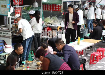XI'AN, CHINA - OCTOBER 9, 2018: Making chinese street food and people eating on small outside tables in Xi'an city, China. Stock Photo