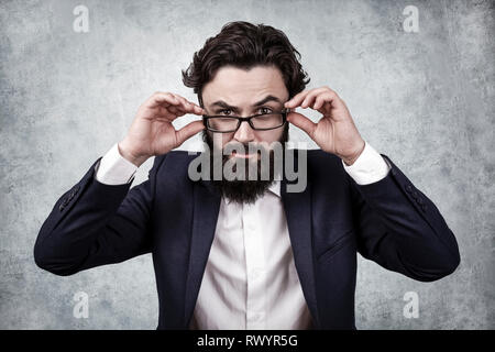 bearded businessman holds the glasses with his hands and frowns at the camera Stock Photo