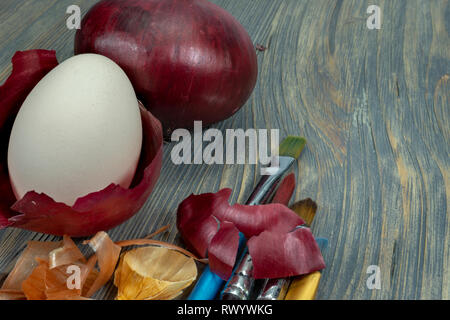 Fresh egg balancing in a dried onion skin, painting brushes and dried onion skin on a wooden table. Easter eggs dyed with onion skins concept Stock Photo